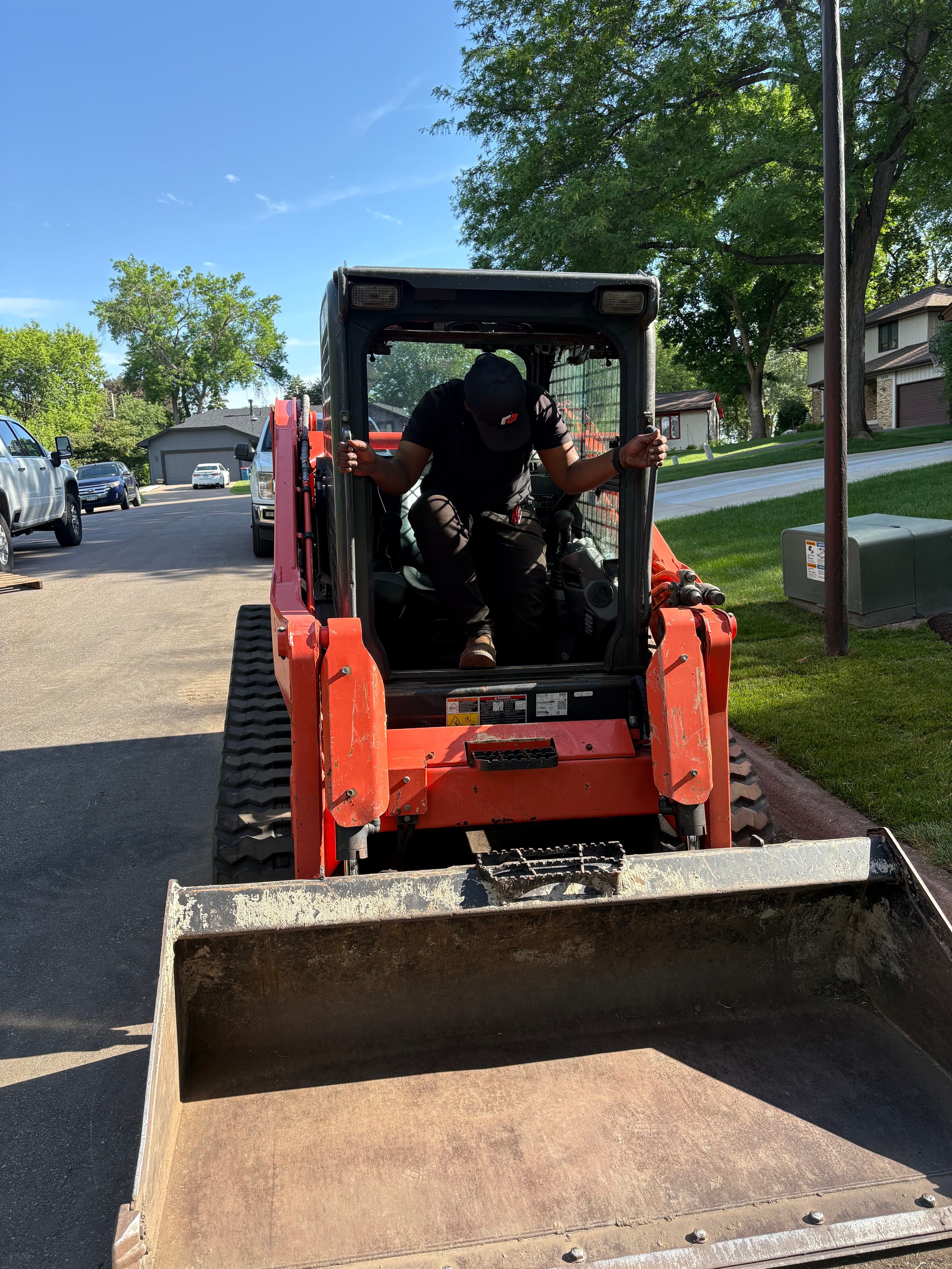 Operator climbing into a red skid steer loader on a residential street.