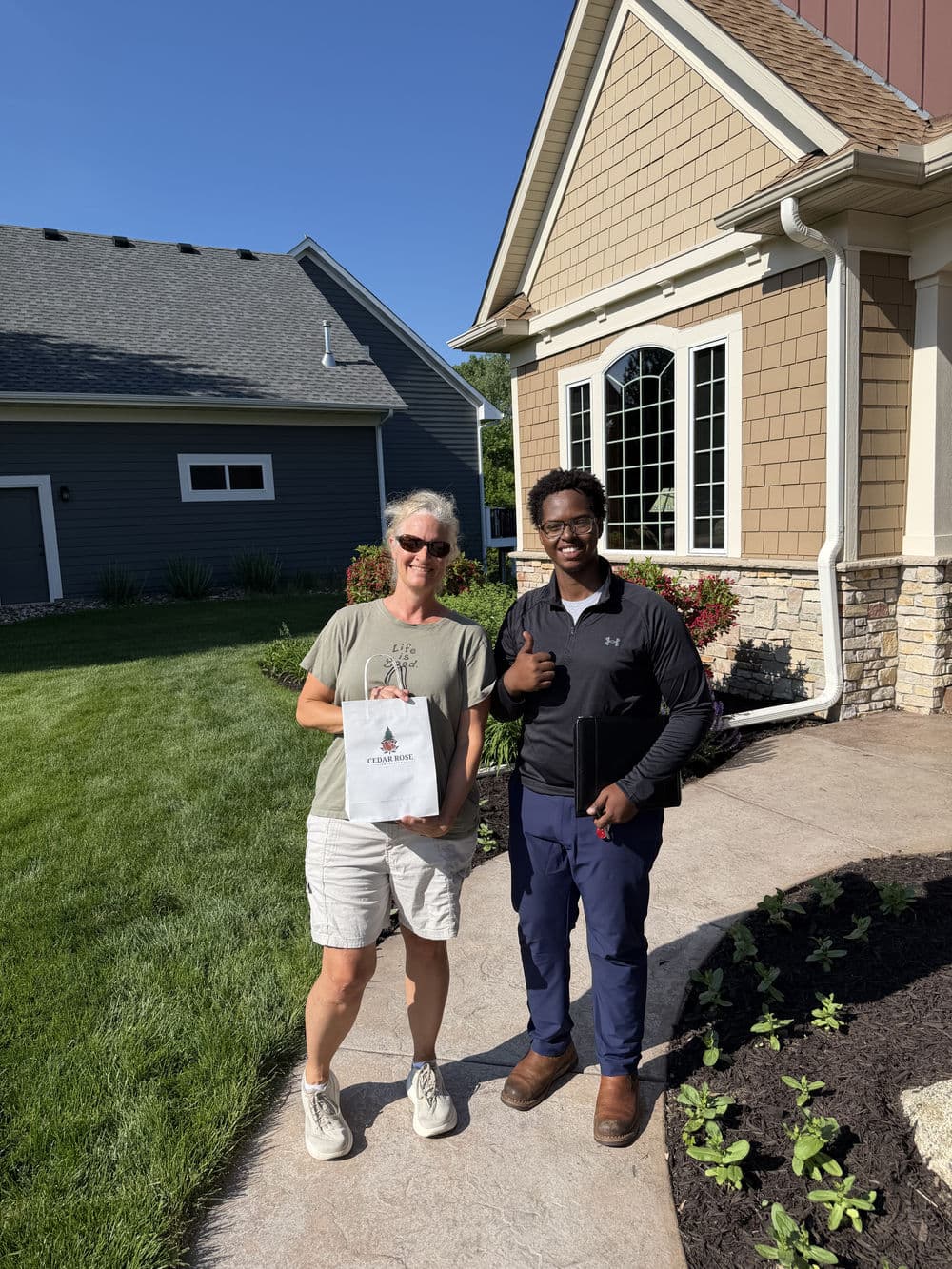 Homeowners receiving landscaping service with certificate outside a house.